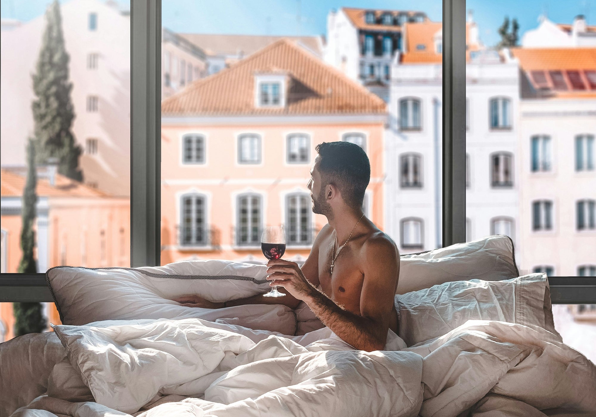 Man sitting on a bed with a cityscape view through large windows