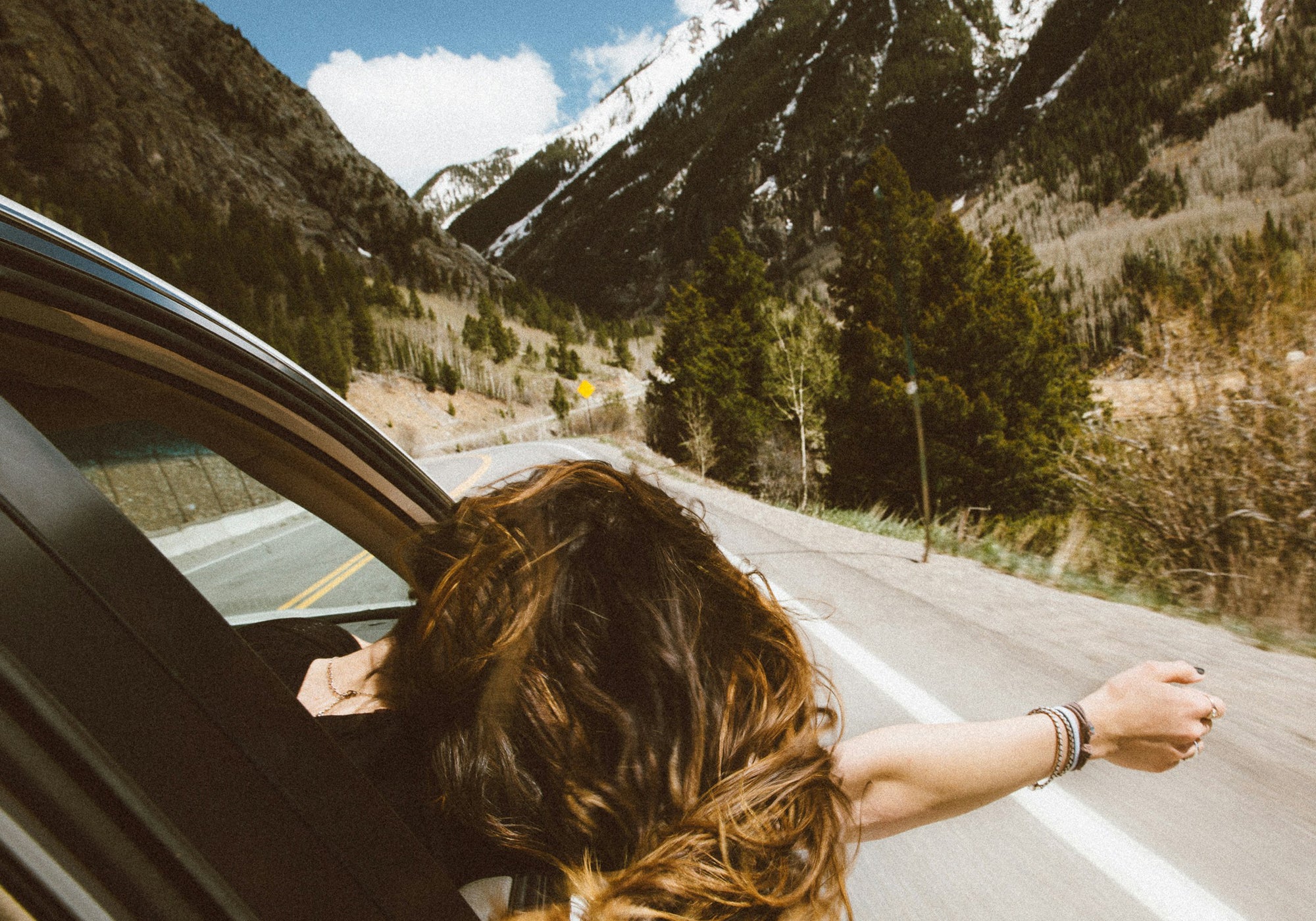 Woman leans out of passenger side window of car feeling the breeze.