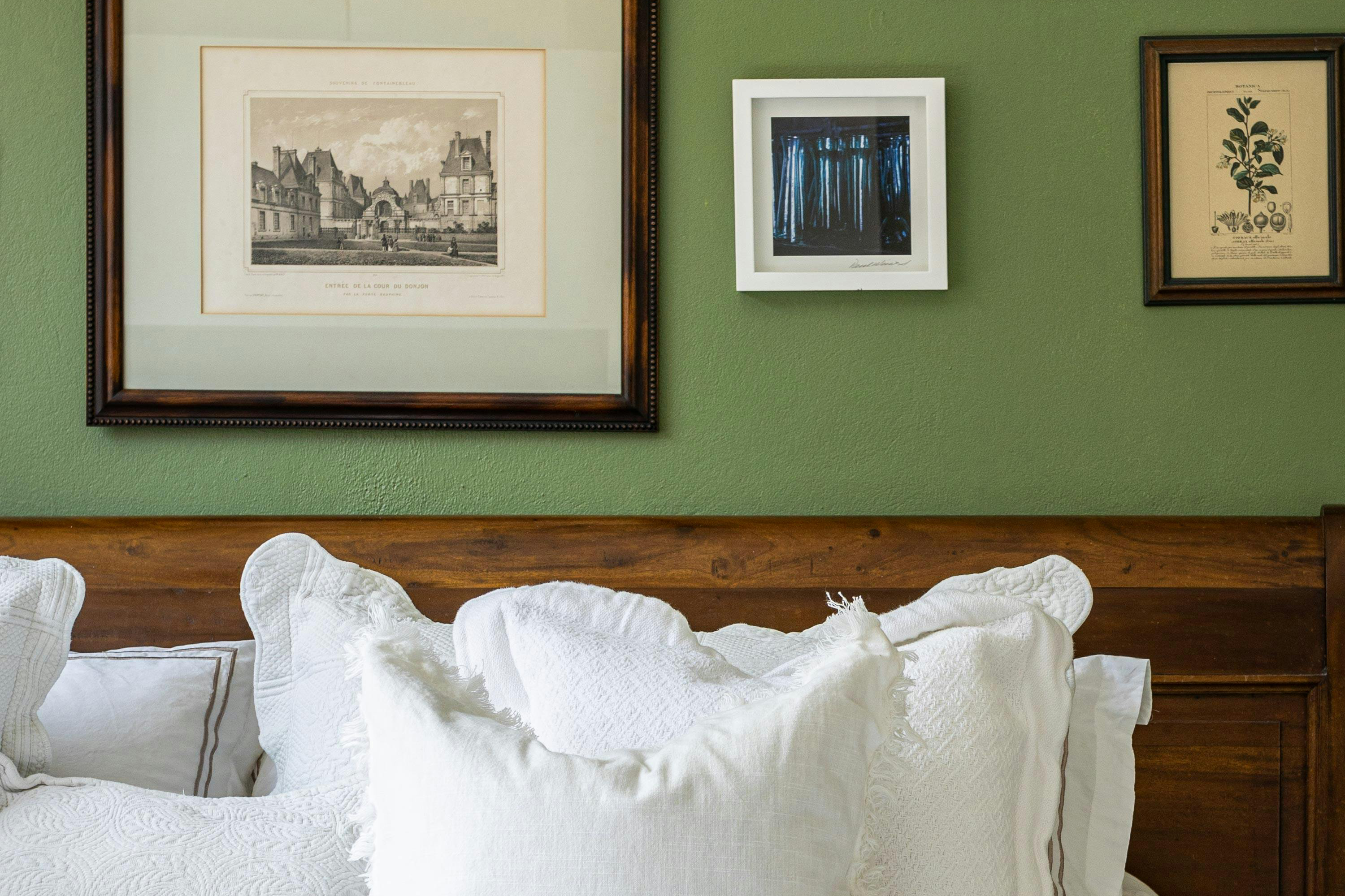 Framed artwork on a green wall above a wooden headboard with white pillows.