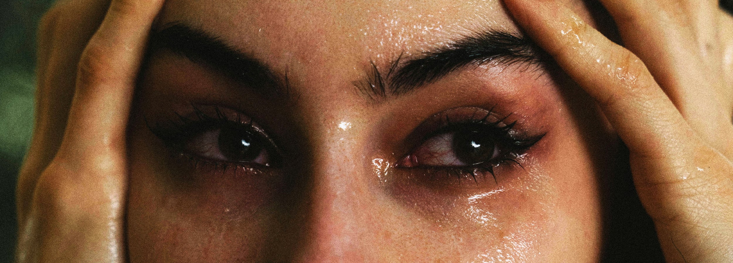 Close-up of a woman's face with hands covering her eyes, showing signs of distress.