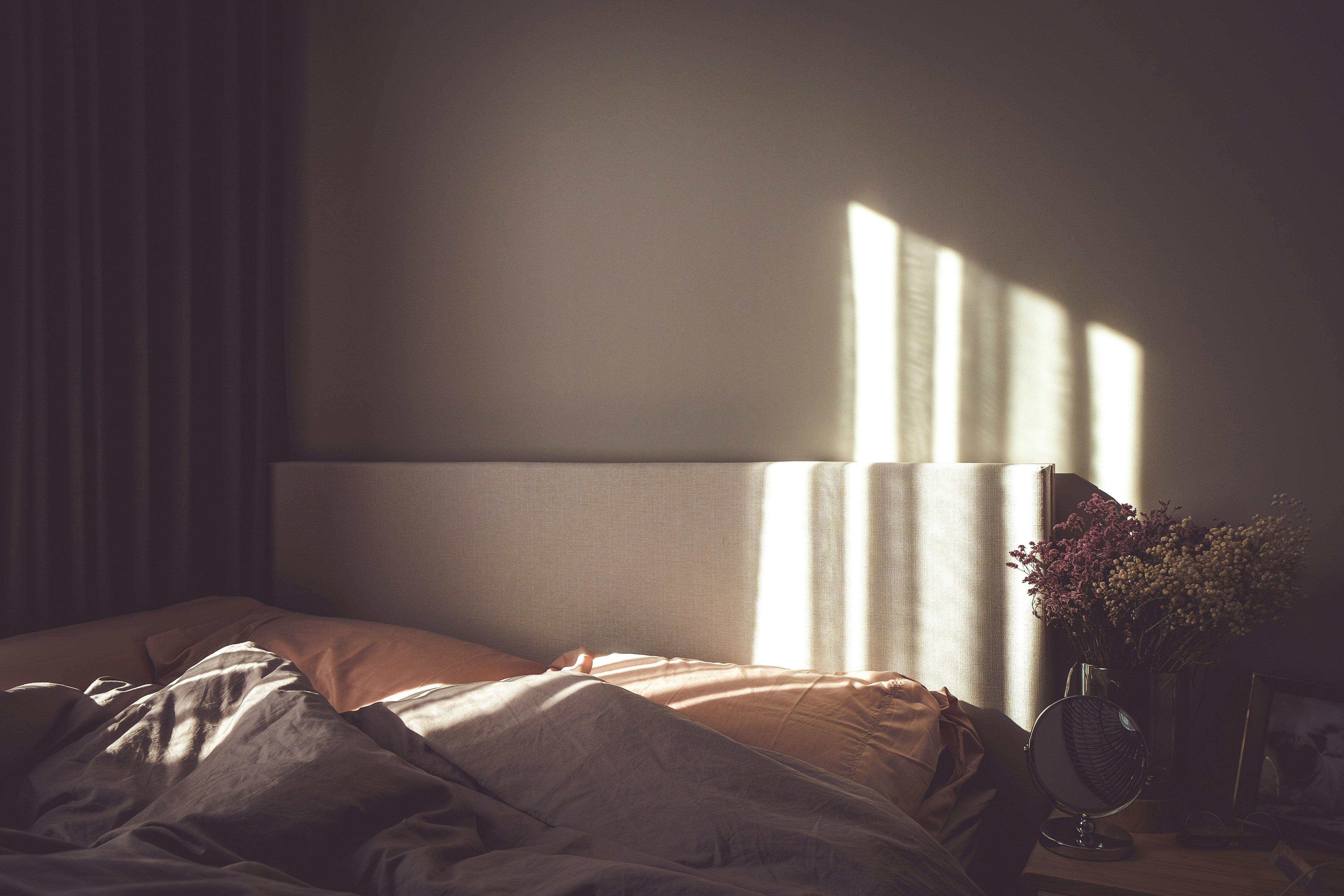 Sunlight filtering through a window casting shadows on a bed in a dimly lit room.