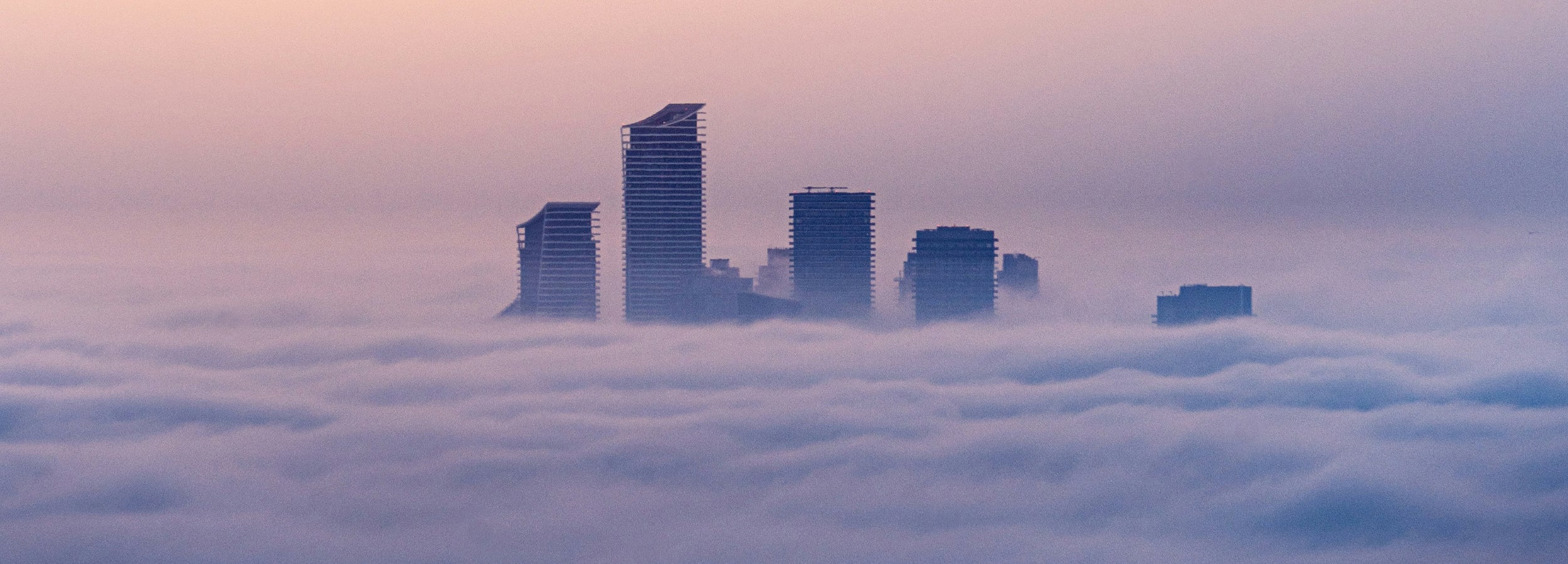 City skyline with tall buildings emerging from a sea of fog at dawn.