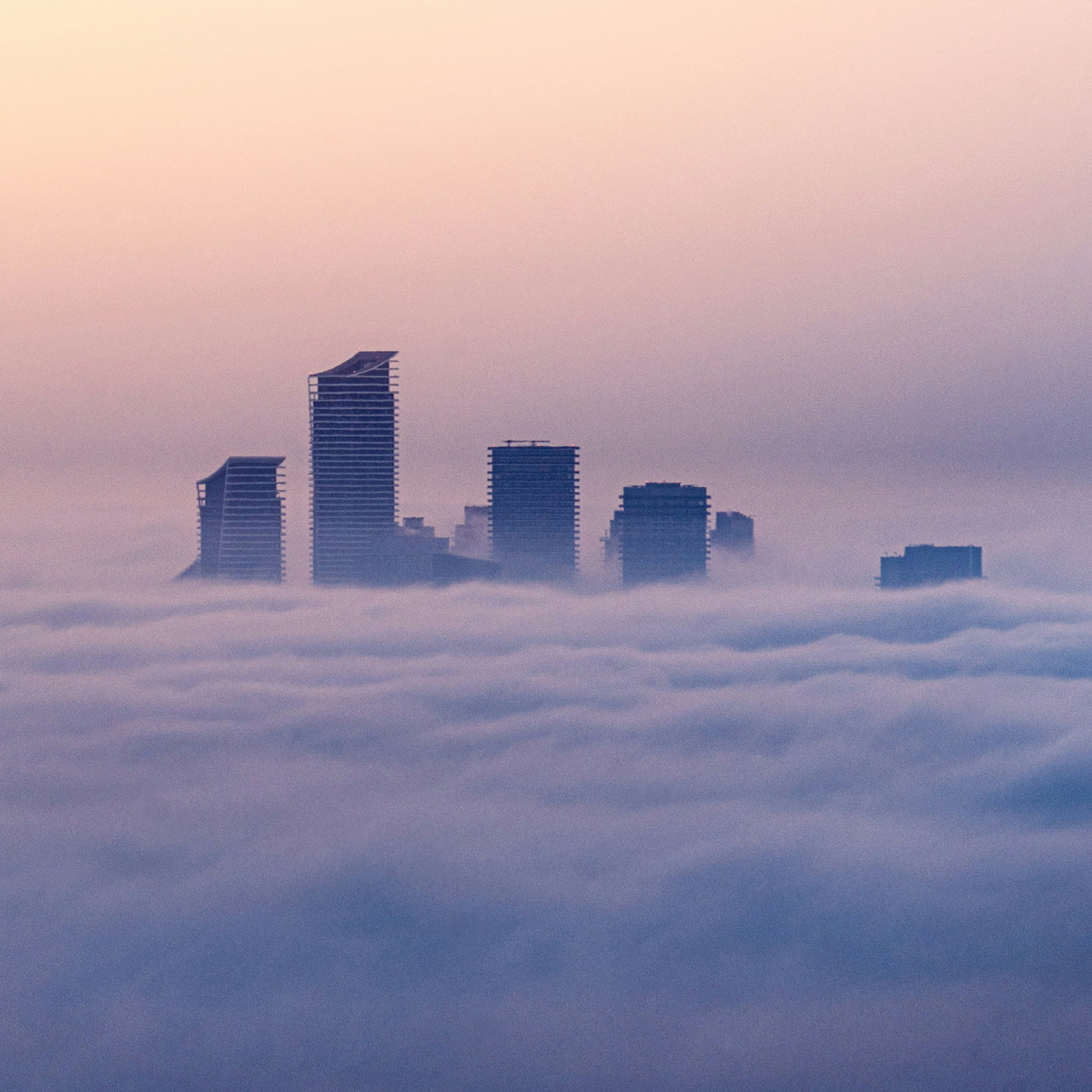City skyline emerging from a sea of fog with a pastel sky.
