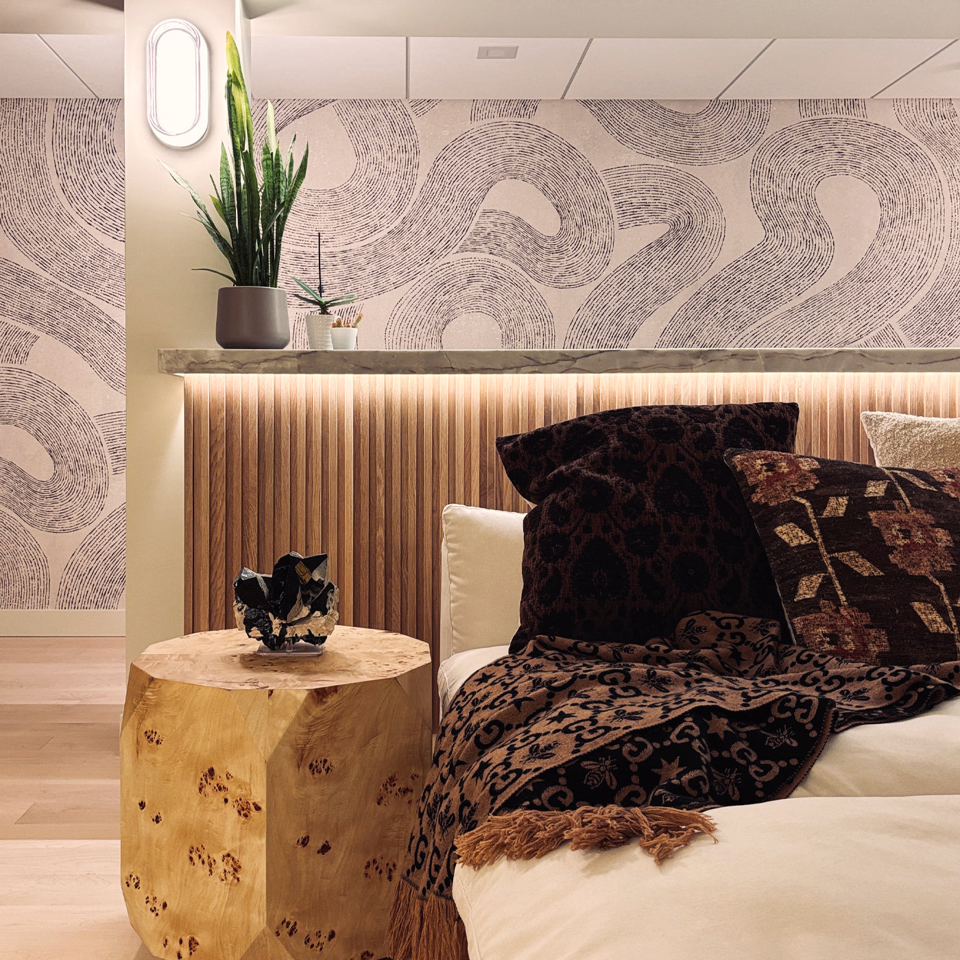 Modern living room with a sectional sofa, side table, and decorative elements. A graphic wallpaper is on the wall in the background.