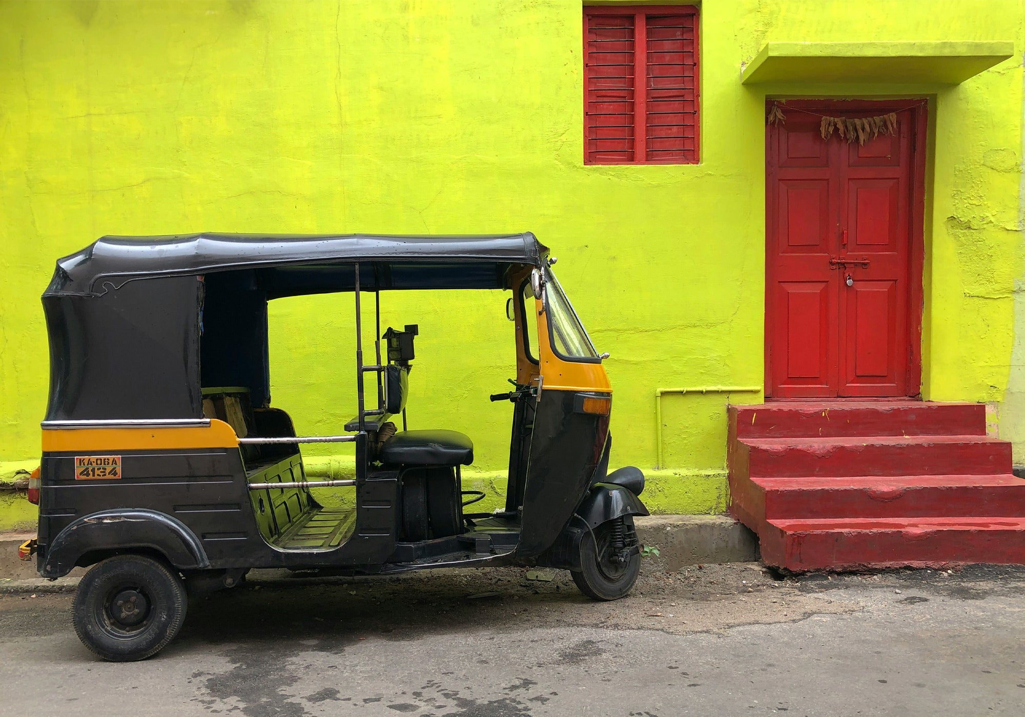 Black auto-rickshaw parked in front of a bright yellow wall with a red door.