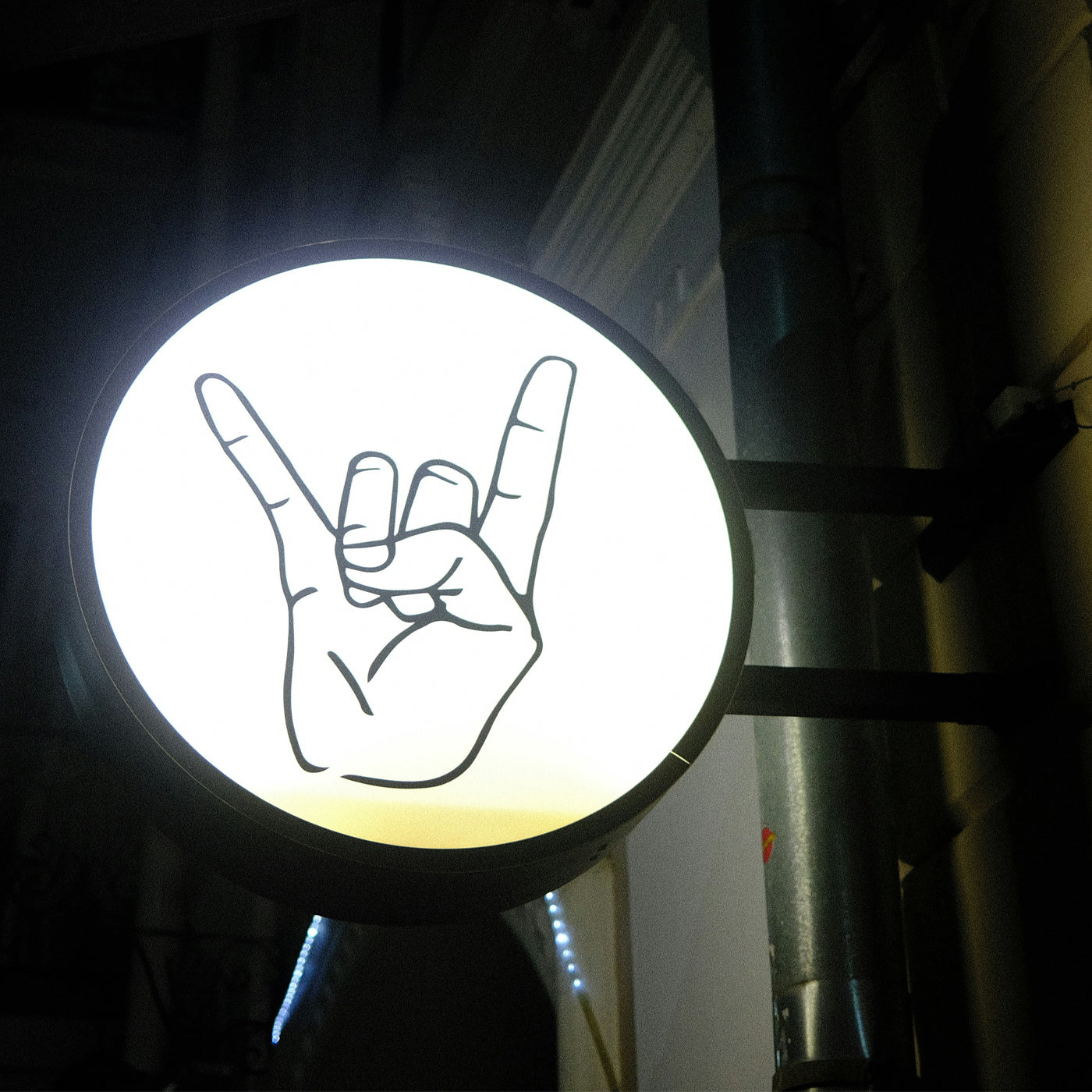Circular storefront sight backlit with a hand making a rock sign.