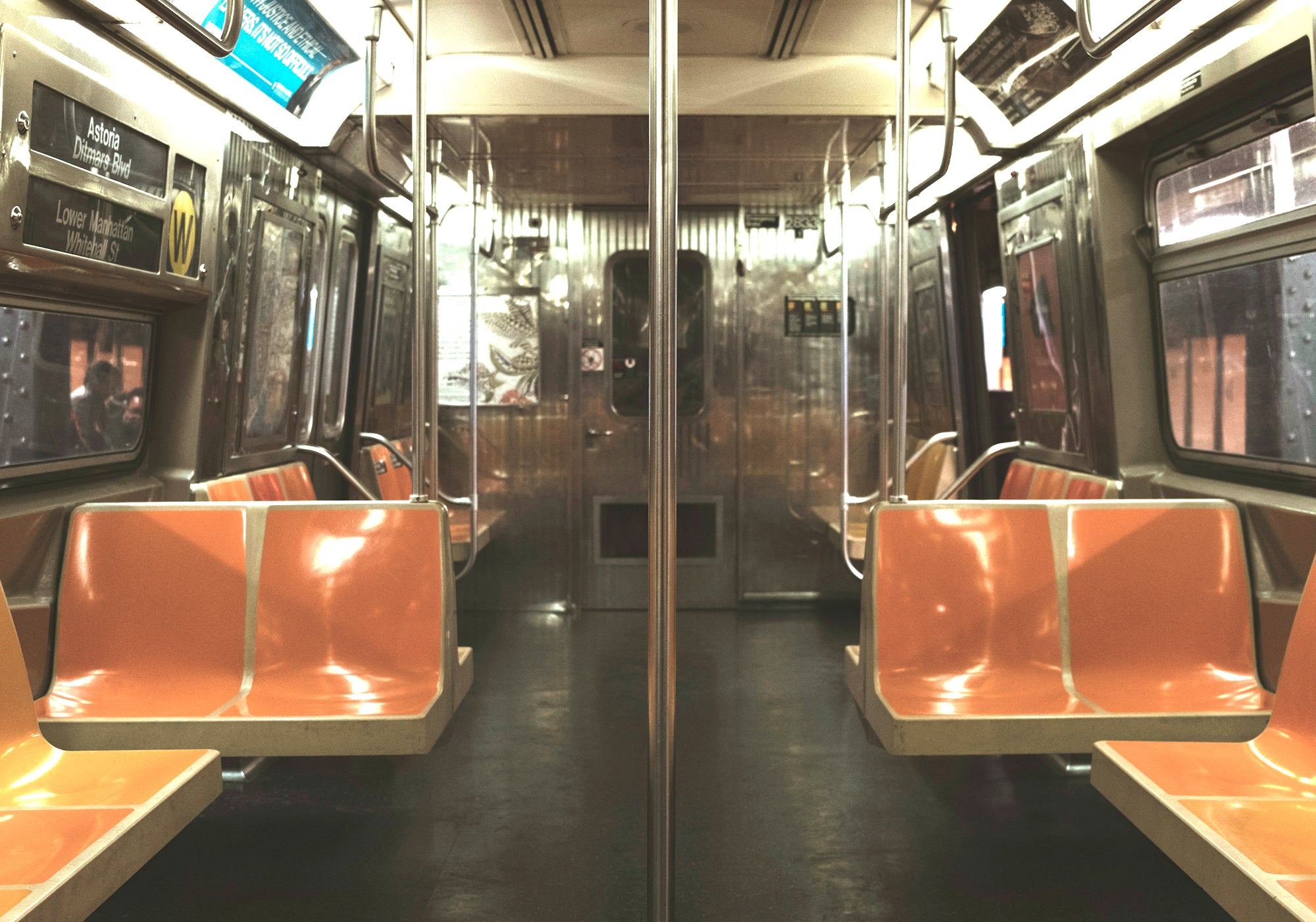 Empty subway car with orange seats and reflective surfaces.