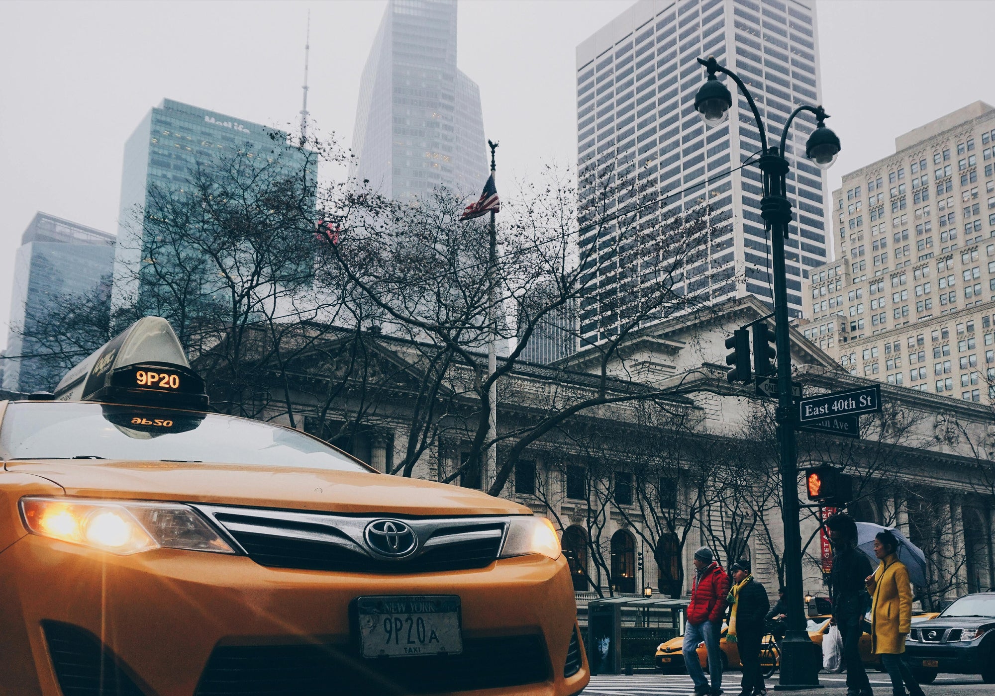Yellow taxi in a city street with tall buildings and pedestrians.