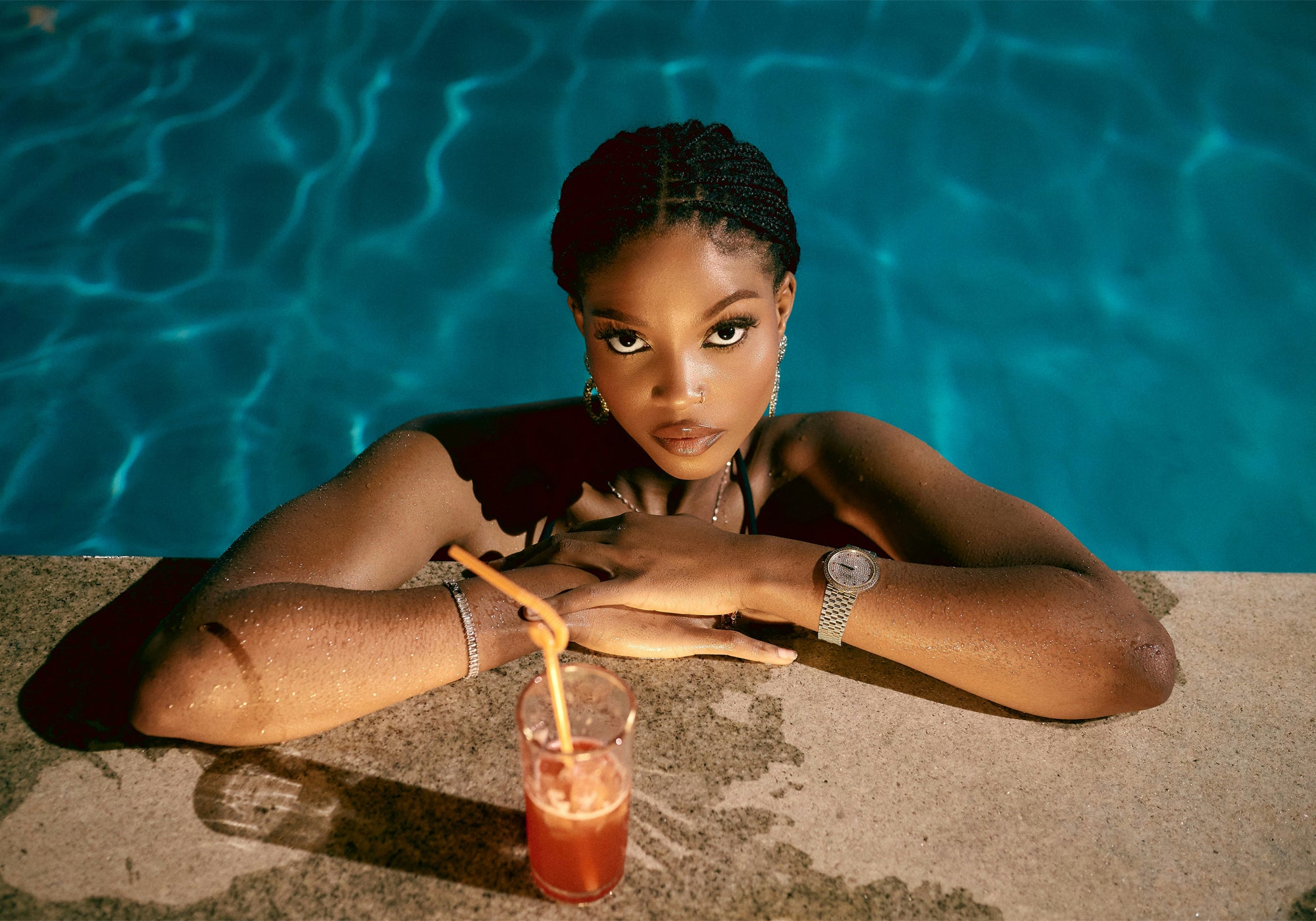 Woman by a pool with a drink, wearing a watch.
